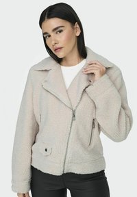 Giacca in fleece color beige chiaro, con zip anteriore, colletto grande, tasche laterali e tessuto testurizzato. Dettagli metallici in tonalità argento.