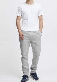 Jasnoszare bawełniane dresy z elastycznym paskiem, bocznymi kieszeniami i prostymi nogawkami, w połączeniu z białym bawełnianym t-shirtem i ciemnymi sneakersami.