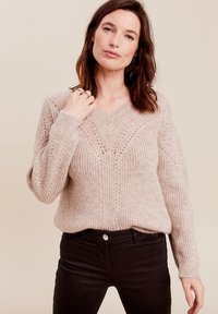 V-ausschnitt Strickpullover in sanftem Beige mit gerippter Textur, featuring ein Zickzackmuster. Lange, leicht taillierte Ärmel und lockere Passform.