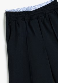 Navyblaue Hose mit elastischem Bund, versehen mit hellblauen Streifen, Seitentaschen, weichem Stoff und entspannter Passform.