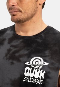 Black tie-dye sleeveless shirt featuring a white spiral graphic and "QUIK SILVER" text. Soft cotton material with a round neckline.