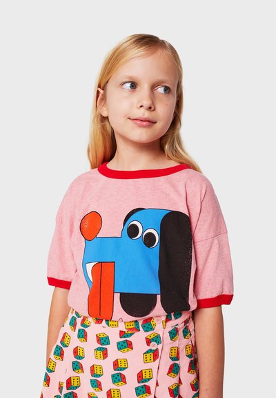 Camiseta rosa con cuello rojo que presenta un gráfico de un perro de dibujos animados en azul. Combinada con una falda de estampado en rosa, amarillo y verde.