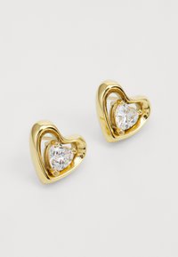 Des boucles d'oreilles en forme de cœur en or présentent une pierre claire et facettée dans un sertissage en griffes, entourée d'un design métallique lisse et fluide.