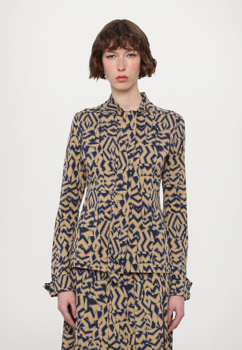 Collared long-sleeve blouse in a navy and beige abstract pattern. Lightweight fabric with a button-down front and ruffled cuffs.