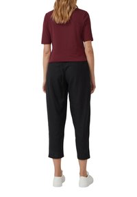 Haut bordeaux à manches courtes associé à un pantalon noir court, avec une coupe décontractée et des baskets blanches. Texture du tissu lisse visible.