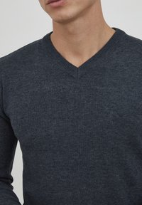 Maglione grigio scuro a collo a v realizzato in un tessuto morbido e strutturato. Presenta un colletto a coste e maniche lunghe attillate.