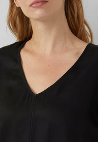 Zwarte V-hals top van een glad, gestructureerd stof met schone naden, die een minimalistisch ontwerp toont.
