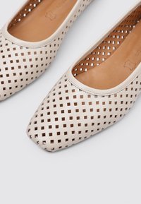 Ballerines perforées beige clair au design à bout carré. Les chaussures présentent un motif carrée découpé et une doublure intérieure lisse marron clair.
