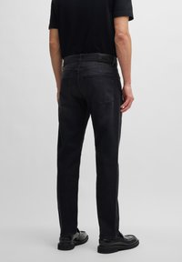 Schwarze Denim-Jeans mit geradem Schnitt, ausgestattet mit zwei Gesäßtaschen und einem Lederlogo-Patch am Bund. Glatte Textur.