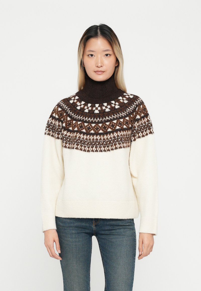 Pulôver de malha com um alto gola alta, apresentando um yoke padronizado em castanho e branco. O corpo principal é de cor creme, com punhos e bainha canelados.