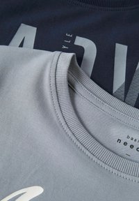 Twee crewneck t-shirts, een marineblauwe en een lichtgrijze, met grote bedrukte tekst en ribgebreide halslijnen. Zacht katoenmateriaal, casual ontwerp.