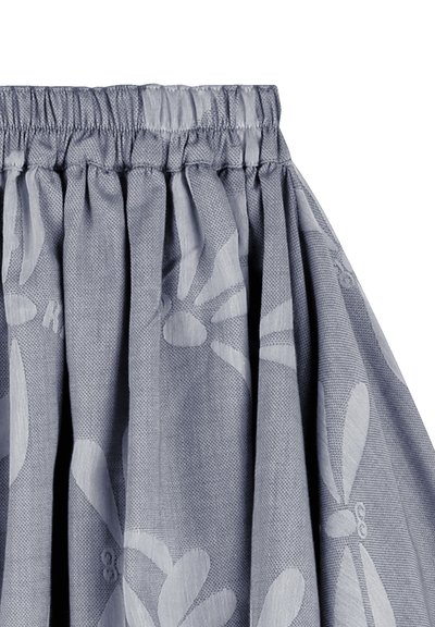Tissu gris clair avec un tissage texturé, présentant un motif floral subtil. La ceinture élastique froncée crée un drapé volumineux.