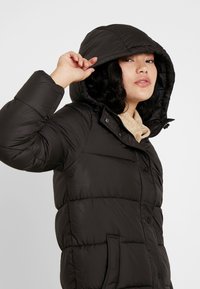 Doudoune noire avec capuche, design matelassé, dotée d'une fermeture éclair à l'avant, de boutons-pression et de poches latérales, avec un doublure intérieure douce.