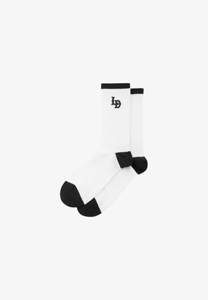 Bele nogavice z črnimi prsti in petami. Imajo rebrasto teksturo in majhen črn logotip ob strani. Narejene so iz mehkega, raztegljivega materiala.