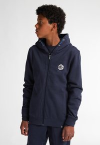 Sudadera con cremallera de color navy, hecha de algodón, que presenta una capucha con cordones y un parche de logo en el pecho, con puños y dobladillo acanalados para un ajuste ceñido.