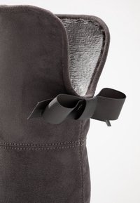 �Šedá semišová bota s plyšovým vnitřkem, zdobená černou stuhovou mašlí a prošitými detaily na boku.
