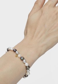 Pulsera de perlas barrocas con diferentes tonos de perlas blancas y grises, intercaladas con un pequeño acento dorado, sobre una muñeca.
