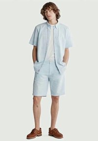 Light blue short-sleeve shirt with button closure, paired with light blue checkered shorts. Brown shoes complete the outfit.