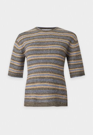 Femme portant un pull rayé à manches courtes, une jupe bleu marine mi-longue, des bottines noires et tenant un sac à main noir sur un fond uni.