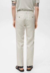 Ljusbeige linnebyxor med rak skärning, utrustade med två bakfickor, och stylade med svarta sandaler. Strukturerad textil med minimal design.