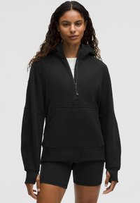 Czarna bluza z kapturem, zapinana na pół zamka, z rękawami raglanowymi i kieszenią na przodzie. Wykonana z miękkiego, strukturalnego materiału.