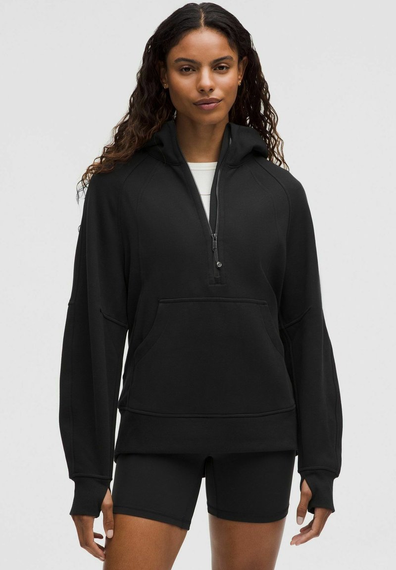 Czarna bluza z kapturem, zapinana na pół zamka, z rękawami raglanowymi i kieszenią na przodzie. Wykonana z miękkiego, strukturalnego materiału.