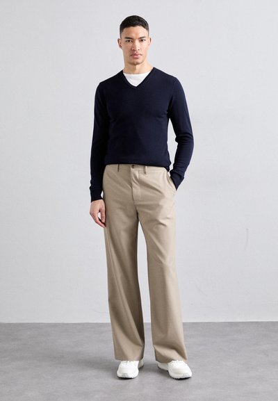 Pull marin à col en V avec des manches longues associé à un pantalon plissé beige clair. Des baskets blanches complètent la tenue, avec un design minimal.