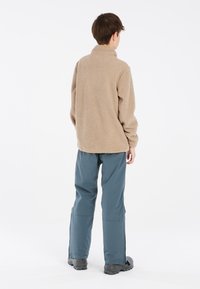 Pulóver de forro polar beige con cuello alto, textura suave. Combinado con pantalones azul oscuro, ligeramente holgados, y calzado negro.
