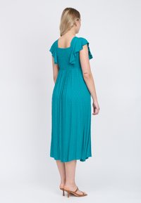 Vestido midi en color teal con mangas cortas acampanadas, cuerpo fruncido y textura de lunares; la tela fluida cae hasta medio pantorrilla.