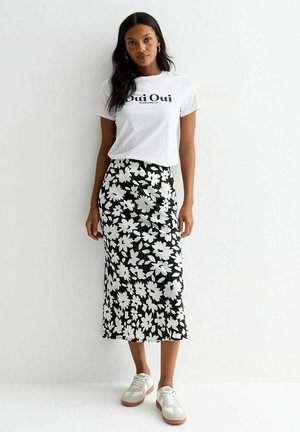 T-shirt blanc avec le texte "Oui Oui", associé à une jupe noire à motif floral. Le footwear comprend des baskets blanches avec une semelle marron clair.