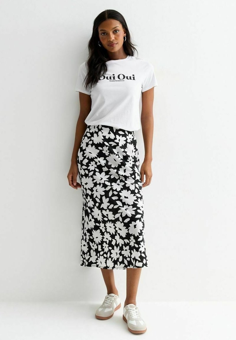 T-shirt blanc avec le texte "Oui Oui", associé à une jupe noire à motif floral. Le footwear comprend des baskets blanches avec une semelle marron clair.