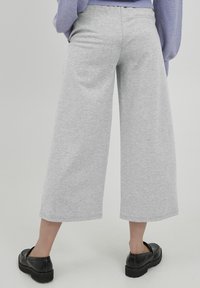Svijetlosive široke trenirke izrađene od mekanog materijala s pojasom. Hlače se protežu do sredine lista i uparene su s crnim cipelama na slip-on.