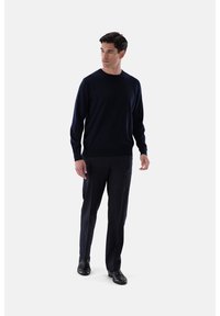 Marineblauer Strickpullover mit langen Ärmeln und Rundhalsausschnitt, kombiniert mit maßgeschneiderten marineblauen Hosen und schwarzen Lederschuhen, zeichnet sich durch eine glatte Textur aus.