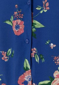 Blå stof med lyserøde og grønne blomstertryk og matchende blå knapper langs en syet søm.