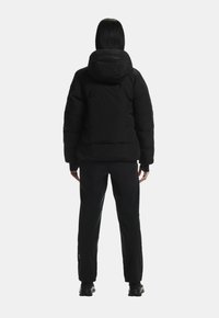 Fekete puff jacket kapucnival, kompakt dizájnnal és varrott részletekkel. Fekete nadrággal és lábbelivel viselve.