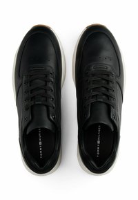 Sneaker in pelle nera con finitura liscia, punta tonda, design con lacci e suola bianca a contrasto. Nome del marchio "Tommy Hilfiger" visibile all'interno.
