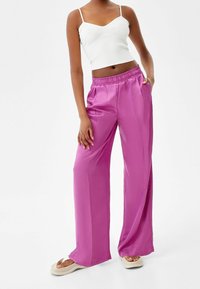 Roze satijnen wijde broek met een elastische tailleband, een soepele textuur en zijzakken, gecombineerd met een nauwsluitend wit geribbeld crop top.