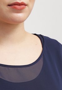 Haut bleu marine avec un col rond et un panneau transparent, texture lisse et coupe confortable, mettant en valeur la zone des épaules et du cou.