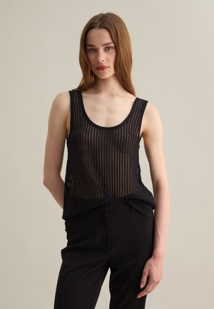 Black sleeveless top featuring a sheer, textured knit pattern. Rounded neckline and slightly loose fit, paired with black pants.