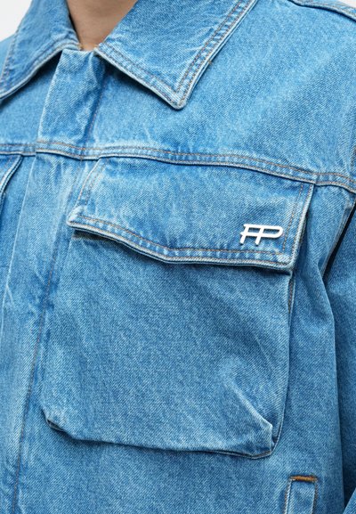 Világoskék farmerrövid kabát klasszikus gallérral, két mellzsebbel és fémlogó díszítéssel. Látható varrásokkal és texturált anyagból készült.