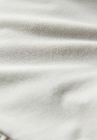 Gros plan sur un tissu doux gris clair avec une texture subtile de tissage diagonal et des plis délicats.