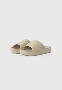 Des sandales à glisser beiges en caoutchouc lisse, avec un large bout ouvert, une semelle plateforme basse et un intérieur texturé pour une meilleure adhérence.
