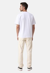 Άσπρο βαμβακερό t-shirt με κοντά μανίκια, συνδυασμένο με ανοιχτό μπεζ παντελόνι. Το σύνολο έχει casual εφαρμογή και απλό σχεδιασμό.