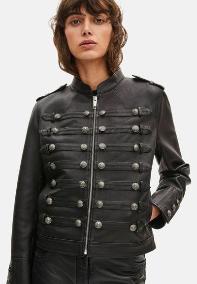 Veste en cuir noir avec col montant, boutons argentés et sangles horizontales de style militaire. Fermeture éclair et coupe ajustée.
