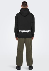 Sudadera negra con capucha, que presenta el texto blanco "Michelangelo" en la parte posterior. Combinada con pantalones cargo verde oliva y calzado negro.
