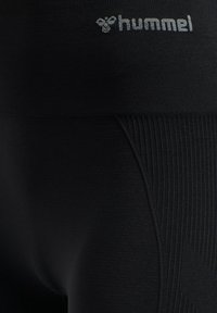 Svart elastiskt tyg med ribbat mönster och "hummel"-logotyp i vitt på midjebandet av träningsleggings eller shorts.