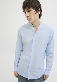 Camisa de manga larga de color azul claro hecha de una tela texturizada, con cuello de banda y cierre de botones, combinada con jeans de mezclilla.