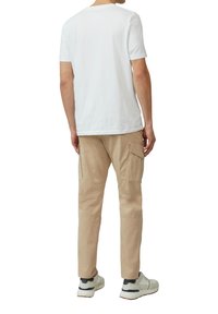 Biała koszulka z krótkim rękawem w połączeniu z beżowymi spodniami cargo z bocznymi kieszeniami. Model w szarych i białych sneakersach.