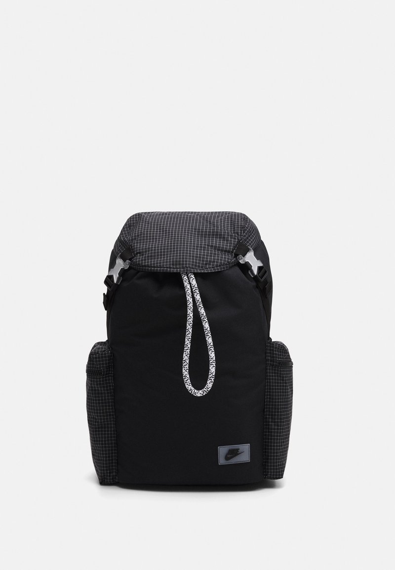 Black backpack with a checkered fabric flap, drawstring closure, and side pockets. Features a small Nike logo on the front.