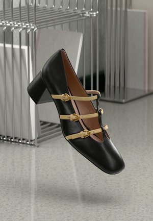 Black leather shoe with a square toe, low block heel, and three yellow straps with gold buckles across the vamp. Smooth texture.